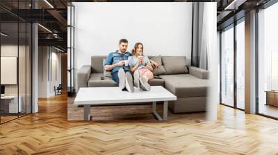 Young couple dressed casually sitting together on the couch and watching TV at home. Wide interior view Wall mural