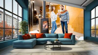 Young couple in sweaters celebrating winter holidays with sparkling wine in the modern house with fireplace Wall mural