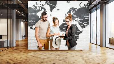 Young couple of travelers choosing a summer strip standing with travel agent on the world map background Wall mural