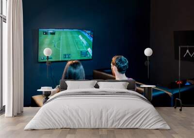 young couple playing football game with gaming console sitting on the couch at the playing club, bac Wall mural