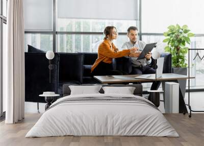 Young couple sitting on the comfortable sofa at the bank or financial institution office, reading an agreement, solving some business or legal affairs Wall mural