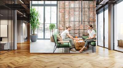 Young couple sitting on the green sofa having vegetarian lunch at the beautiful interior with big window on brick wall Wall mural