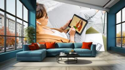 Young creative woman working as a web designer or artist, drawing on a digital tablet while sitting on the comfortable sofa at home Wall mural