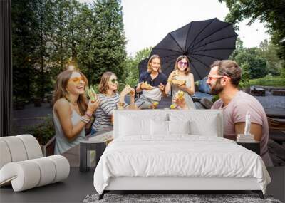 Young friends having fun sitting together with tasty snacks and drinks during the evening lights at the park cafe outdoors Wall mural