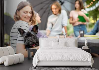 Young friends having fun together sitting with french bulldog during a studying outdoors in the park Wall mural