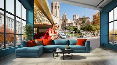 Young happy woman tourist in red dress having excursion in the open touristic bus in Valencia city, Spain Wall mural