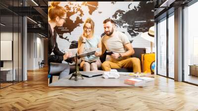 young lovely couple sitting with manager at the travel agency office prepairing for a summer vacatio Wall mural