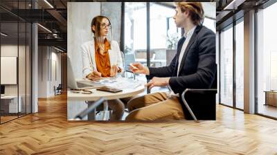 Young man and woman having a serious business conversation, working with paper documents and computer in the office Wall mural