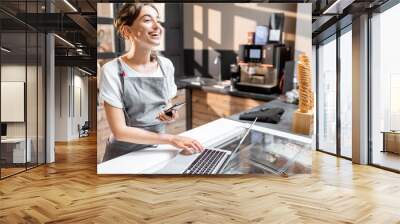 Young saleswoman working with laptop at the counter in ice cream shop or cafe. Concept of a small business and retail Wall mural