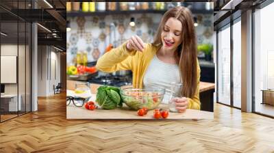 Young smiling woman making healthy fresh salad in the modern kitchen interior full of fruits and vegetables Wall mural