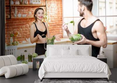 Young sports couple having snack with healthy salad and green smoothie on the kitchen at home Wall mural