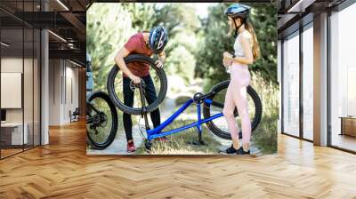 Young sports couple repairing bicycle on the forest road near the car, having a good time during the summer outdoor activities Wall mural