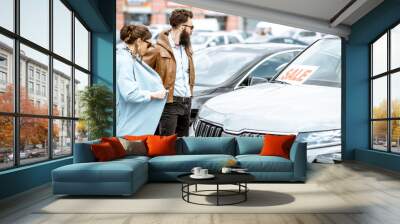 Young stylish couple choosing luxury car to buy on the open ground of the dealership Wall mural