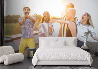 Young stylish friends have fun, shooting confetti during some celebration at rooftop terrace on a sunset Wall mural