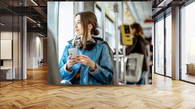 Young stylish woman using public transport, sitting with phone and headphones in the modern tram Wall mural