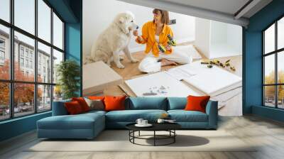 Young woman assembles furniture by herself, sitting and having fun with her cute dog at new apartment. DIY and house improvement concept Wall mural