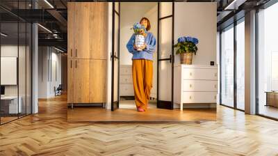 Young woman carries flowers in vase, decorating kitchen interior with fresh flowers or having some household chores Wall mural