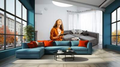 Young woman controlling home light with a digital tablet in the living room. Concept of a smart home and light control with mobile devices Wall mural