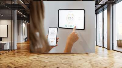 Young woman controlling temperature in the living room with smart phone and digital touch screen panel. Concept of heating control in a smart home Wall mural