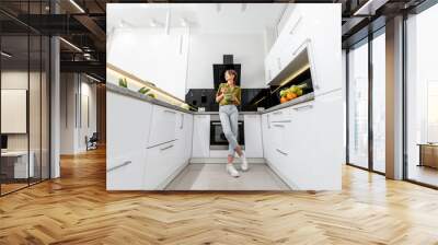 Young woman eating healthy salad on the kitchen at home, wide angle view on the modern white interior Wall mural