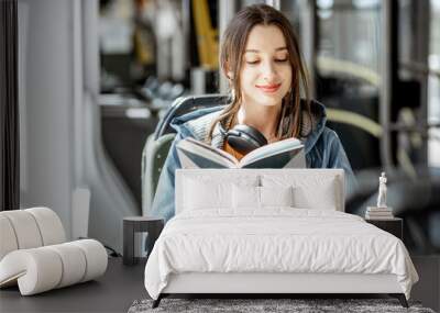 Young woman reading book while moving in the modern tram, happy passenger at the public transport Wall mural