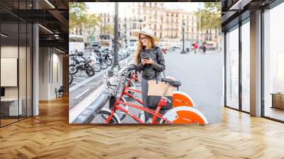 Young woman tourist renting a city bicycle with smartphone in Barcelona Wall mural