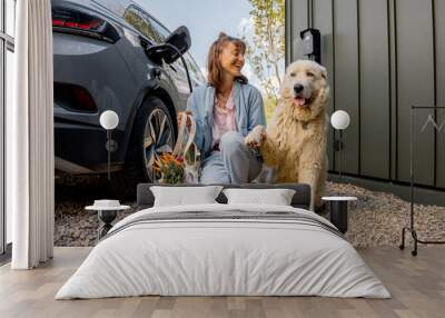 Young woman with her cute white dog sitting together, arrived home by electric vehicle with fresh groceries in bag. Happy and sustainable lifestyle, wellbeing, friendship with pets Wall mural