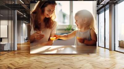 A small child shares an apricot with his mother. Mother and child spend time in sunny kitchen Wall mural