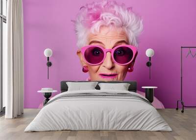 Beautiful elderly fashionable woman in stylish pink clothes and glasses posing on a pink background. Woman looking at the camera in surprise Wall mural