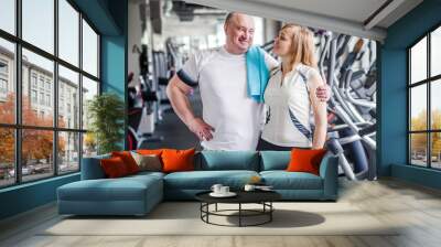 Happy older married couple in the gym. Hugs and looks at the camera Wall mural