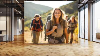 Smiling woman hiker with backpack looking at camera with group of friends hikers rises to the top of the hill Wall mural