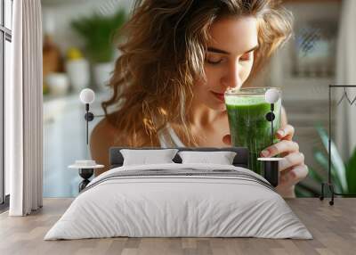 Young Woman Enjoying a Fresh Spirulina Smoothie. A woman is savoring the taste of a green spirulina smoothie in a well-lit, cozy kitchen setting. Horizontal photo Wall mural