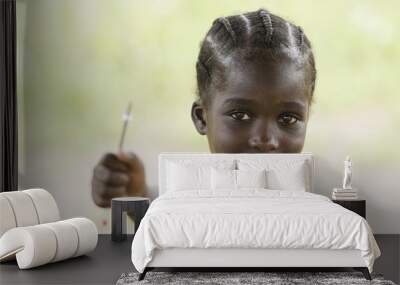 Education symbol: little African black teenage girl holding pen in the air lightly smiling to the camera. African children need education since it is the most important thing for a better future. Wall mural