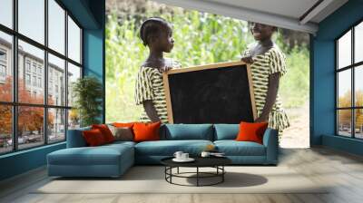 Two Gorgeous African Girls Holding Up a Chalkboard Copy Space. Beautiful girls holding up and showing a black blackboard. Plenty of copy space to add your text. Two black schoolgirls holding a symbol. Wall mural