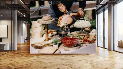 a table in the welcome area with snacks and decor where a person is thinly slicing a large ham Wall mural