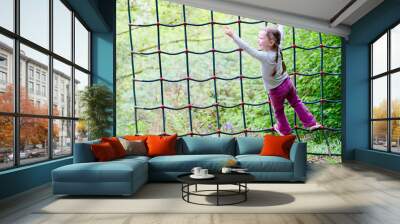 Young girl climbing on rope net frame in outdoor woodland adventure parkground Wall mural