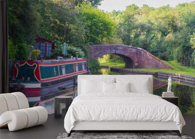 A canal boat or barge moored on the water with a bridge and reflection behind Wall mural