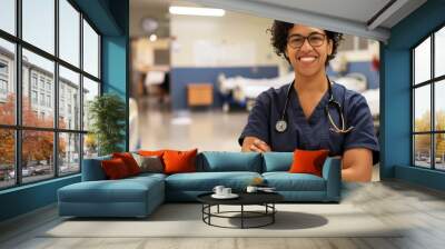 Wearing electric blue eyewear, the nurse stands in the hospital hallway, arms crossed, smiling, and sharing a warm thumbup gesture with a hardwood flooring background Wall mural