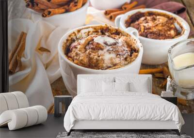 Cinnabon cake in mug. Fast simple microwave dessert idea, background for recipe. Cinnamon roll mugcake, with sugar and cream cheese topping, in different mugs, with cinnamon sticks on wooden backgroun Wall mural