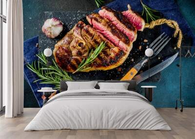 Sliced grilled roast beef with fork for meat and wine on wooden cutting board. Dark blue background. Top view copy space Wall mural