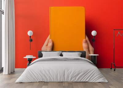 two hands holding blank orange book isolated on red background, made with generative ai Wall mural