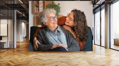 Grandmother and granddaughter laughing and embracing at home Wall mural