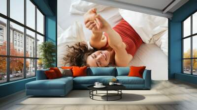 Happy smiling woman stretching on bed in the morning Wall mural