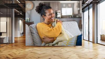 Joyful african woman with blanket on couch laughing Wall mural