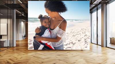 Lovely black woman hugging child with towel at beach Wall mural