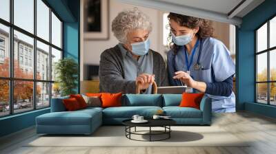 Senior woman and nurse using digital tablet at home during consult Wall mural