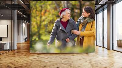 Senior woman walking with granddaughter in park during autumn Wall mural