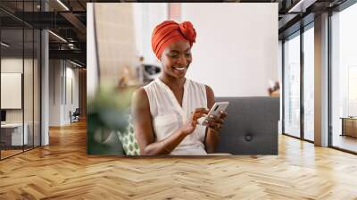 Smiling black woman with african turban using smartphone at home Wall mural