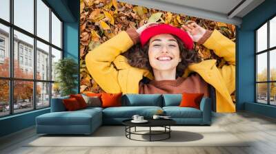 Smiling woman lying on autumn leaves Wall mural