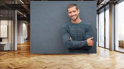 Smiling young man leaning against grey wall Wall mural